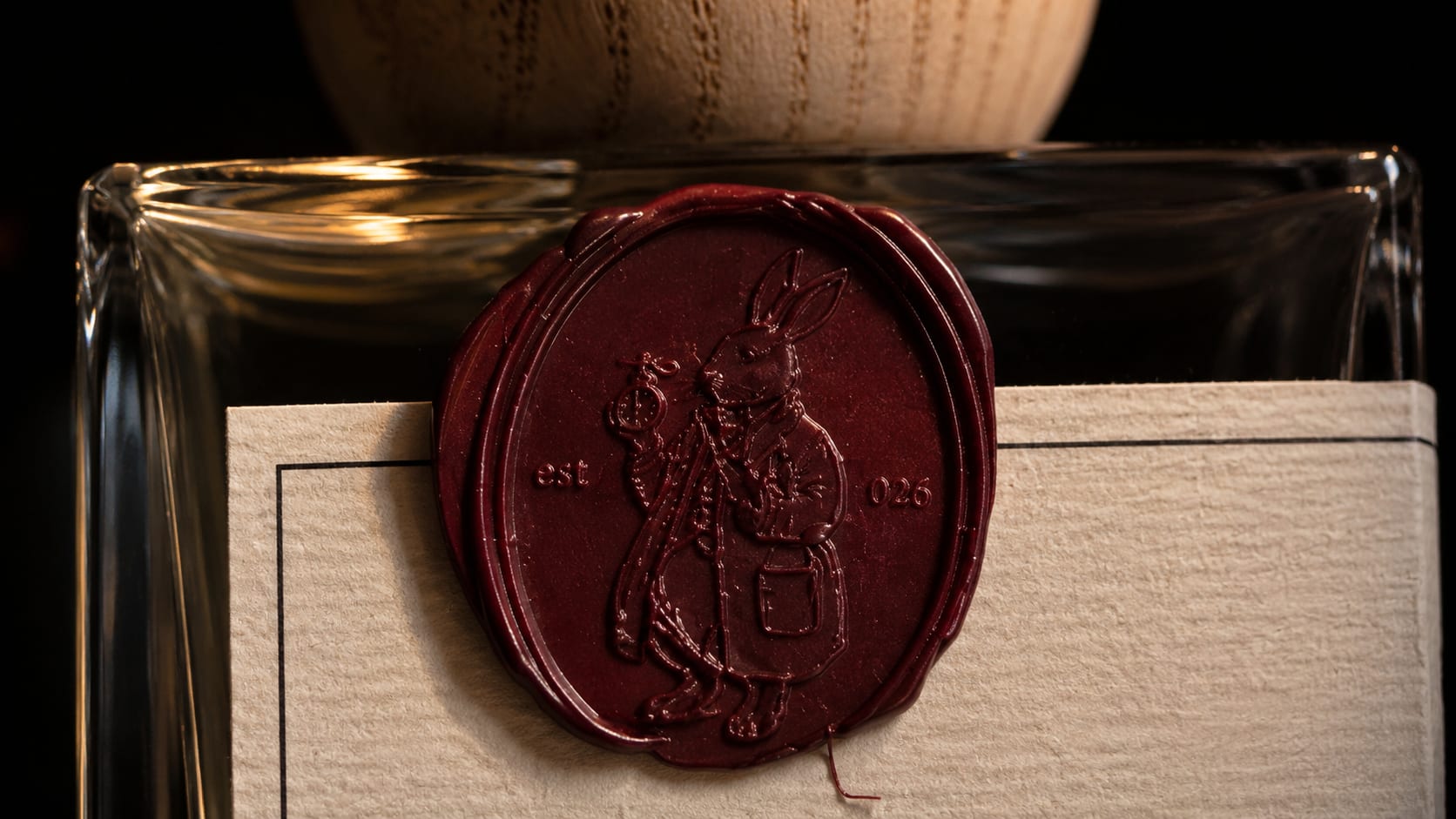 Macro of the burgundy wax seal pressed on the bottle neck, the engraved rabbit perfumer and est 026 legible in the wax.